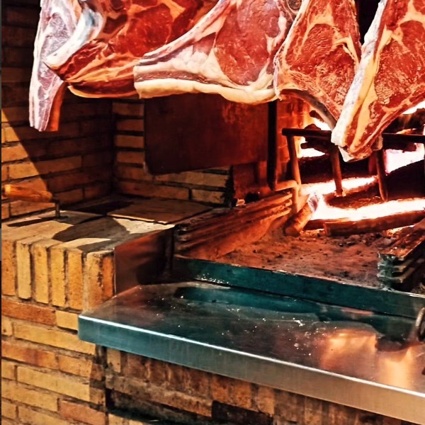Chuletones colgados junto al fuego de la parrilla