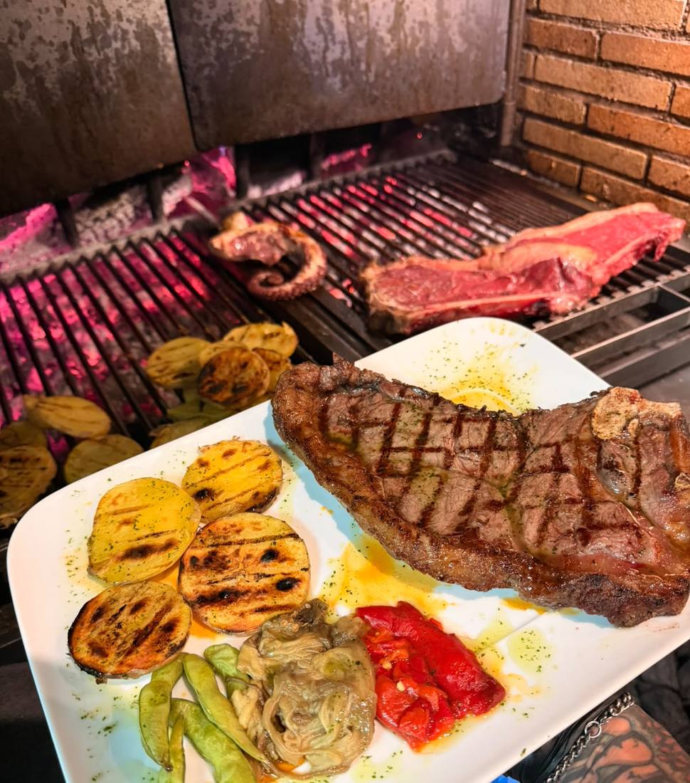Xuletó a la brasa con patata al caliu y verduras, con la parrilla al fondo